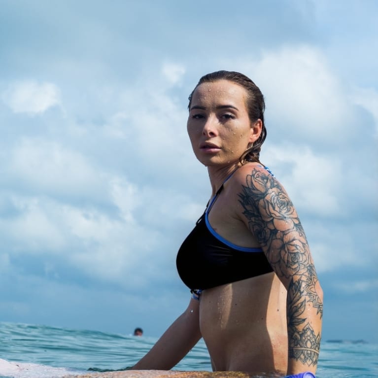A woman wearing a black bikini, sitting on a surfboard in calm ocean waters