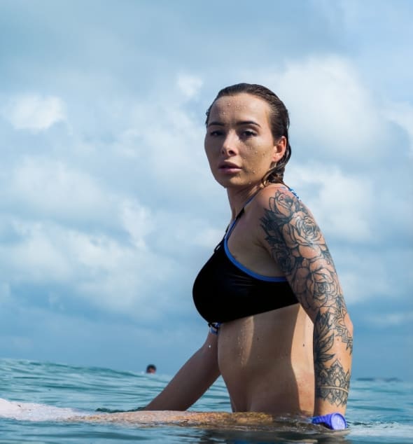 A woman wearing a black bikini, sitting on a surfboard in calm ocean waters