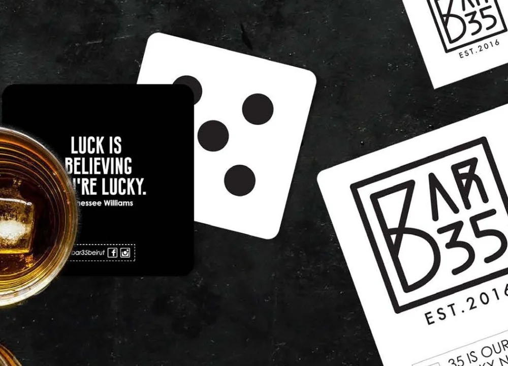 Bar 35 coasters: a black coaster with a line about luck, a white coaster with the boxed logo, and a die on the bar top