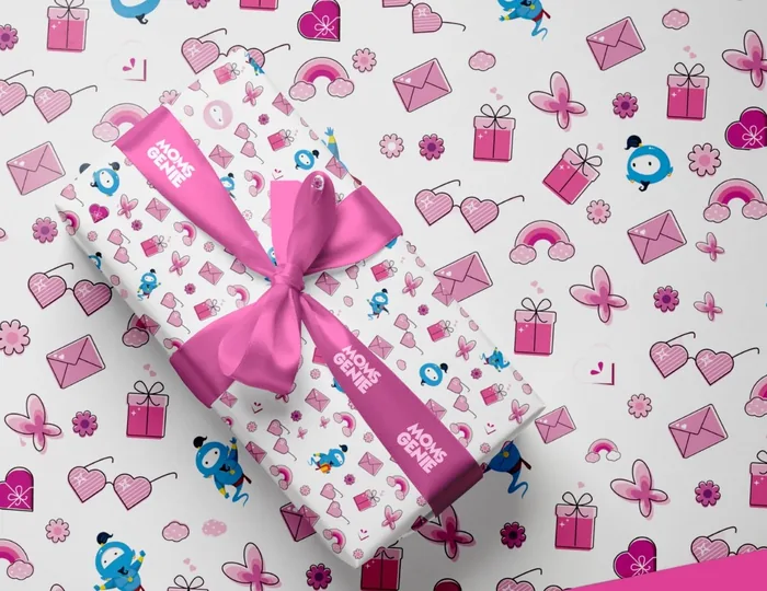 A gift wrapped in MomsGenie paper patterned with Wishie, hearts and presents, tied with a pink ribbon