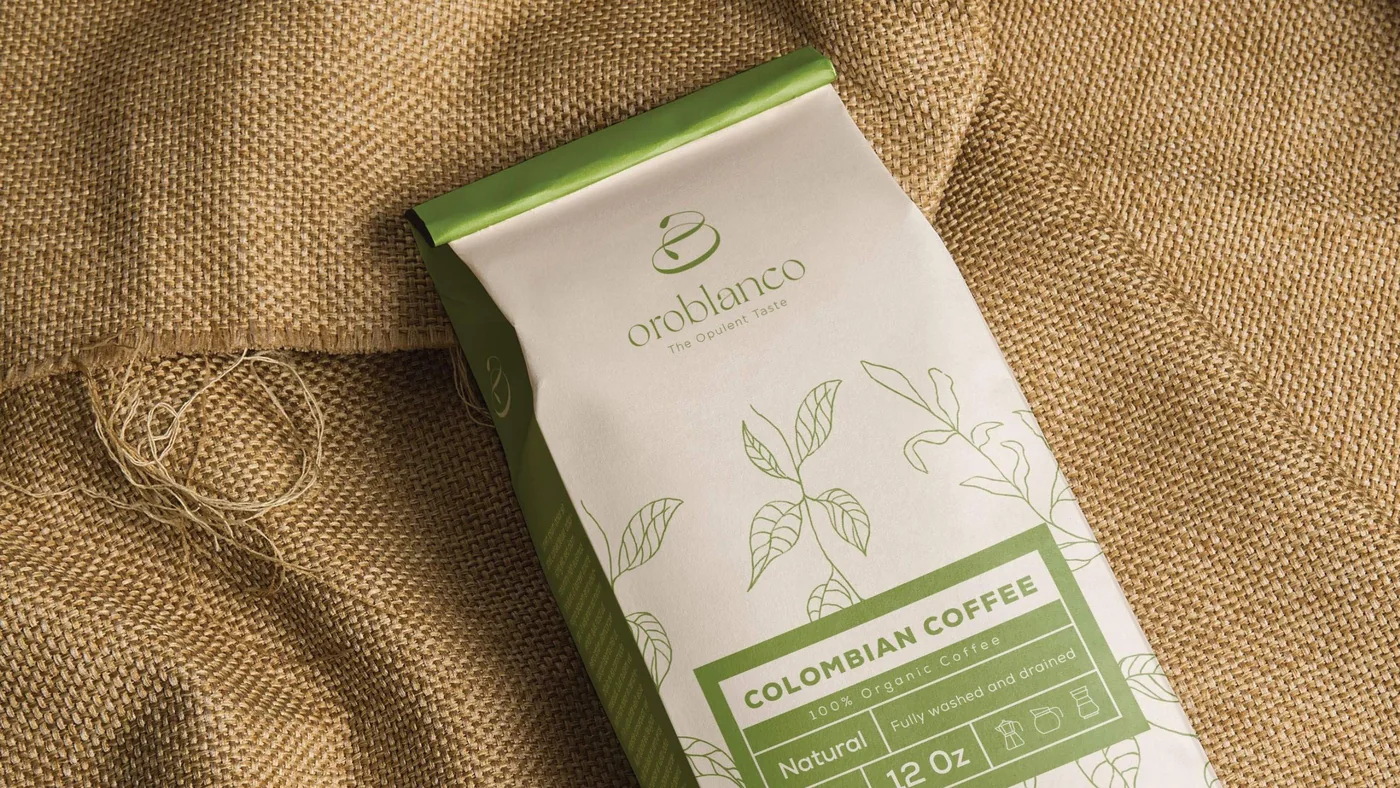 An Oroblanco coffee bag on burlap: cream paper with fine green drawings of coffee branches, the logo, and a green label panel