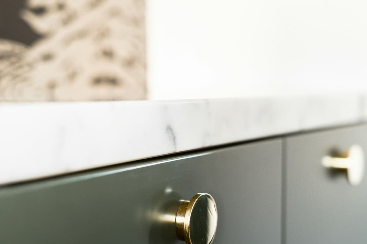 Brass knob on a dark green cabinet below a marble counter