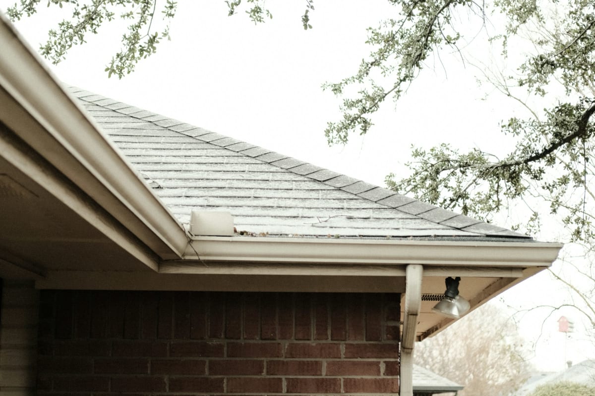White gutter along a shingle roof on a brick home