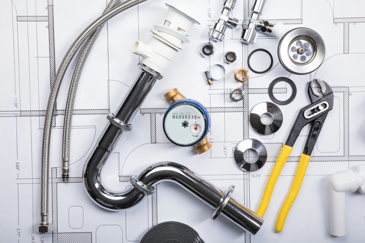 Plumbing parts, pipe and pliers laid out on plans