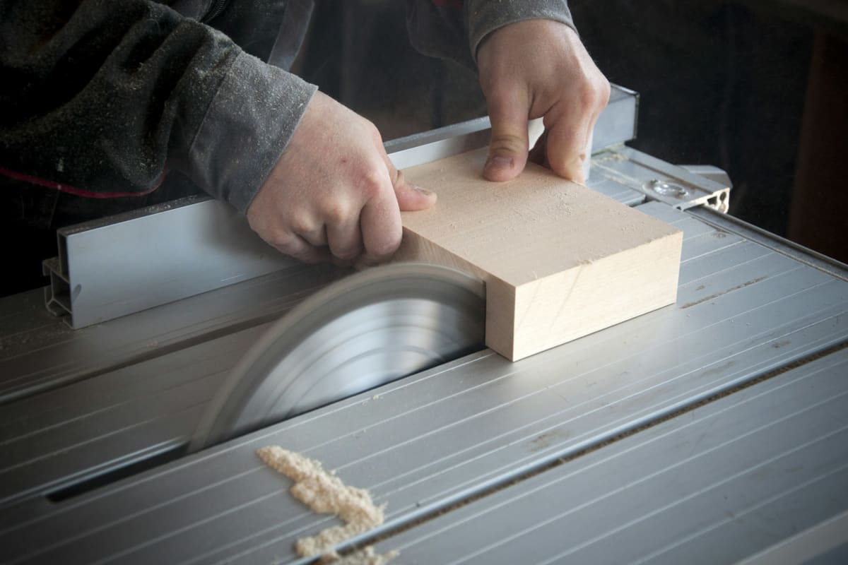 Hands feeding a block through a table saw