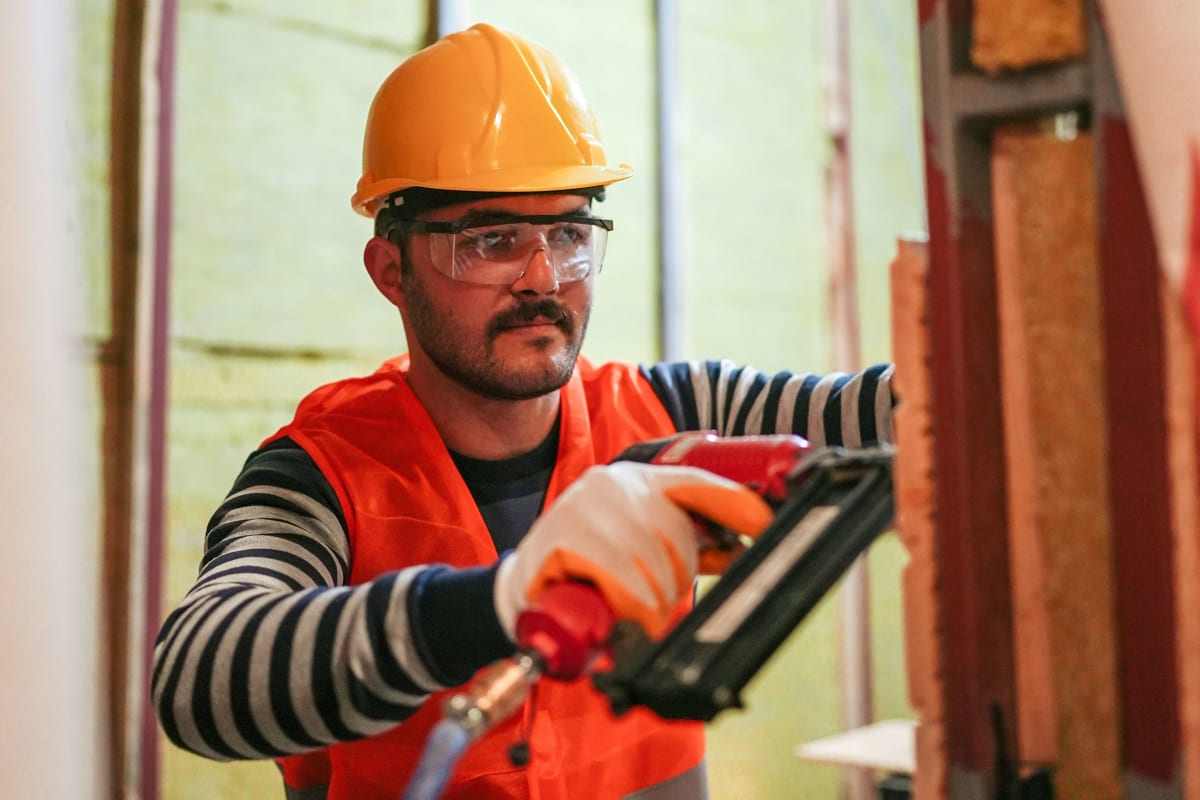 Worker in a hard hat driving nails with a framing nailer