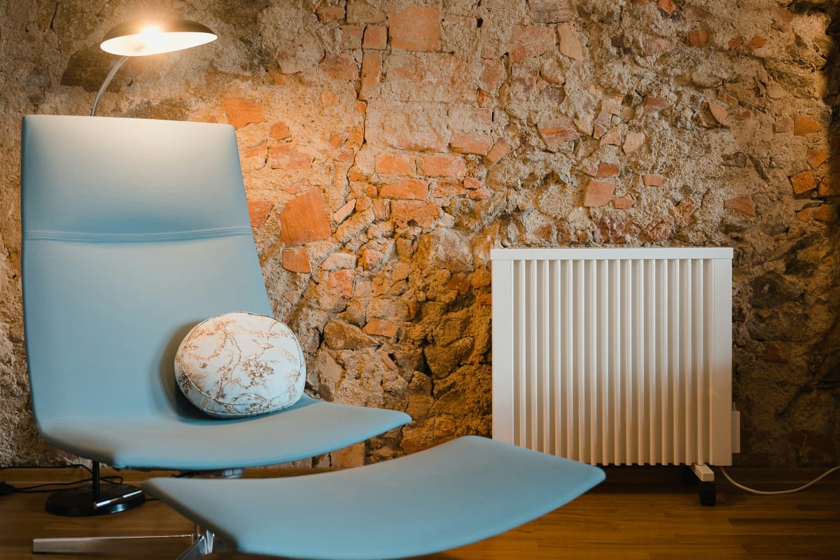 White electric heater beside a lounge chair in a stone-walled room