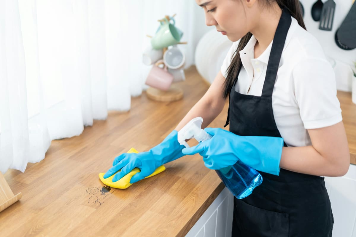 Wiping down a wood counter with spray cleaner and gloves