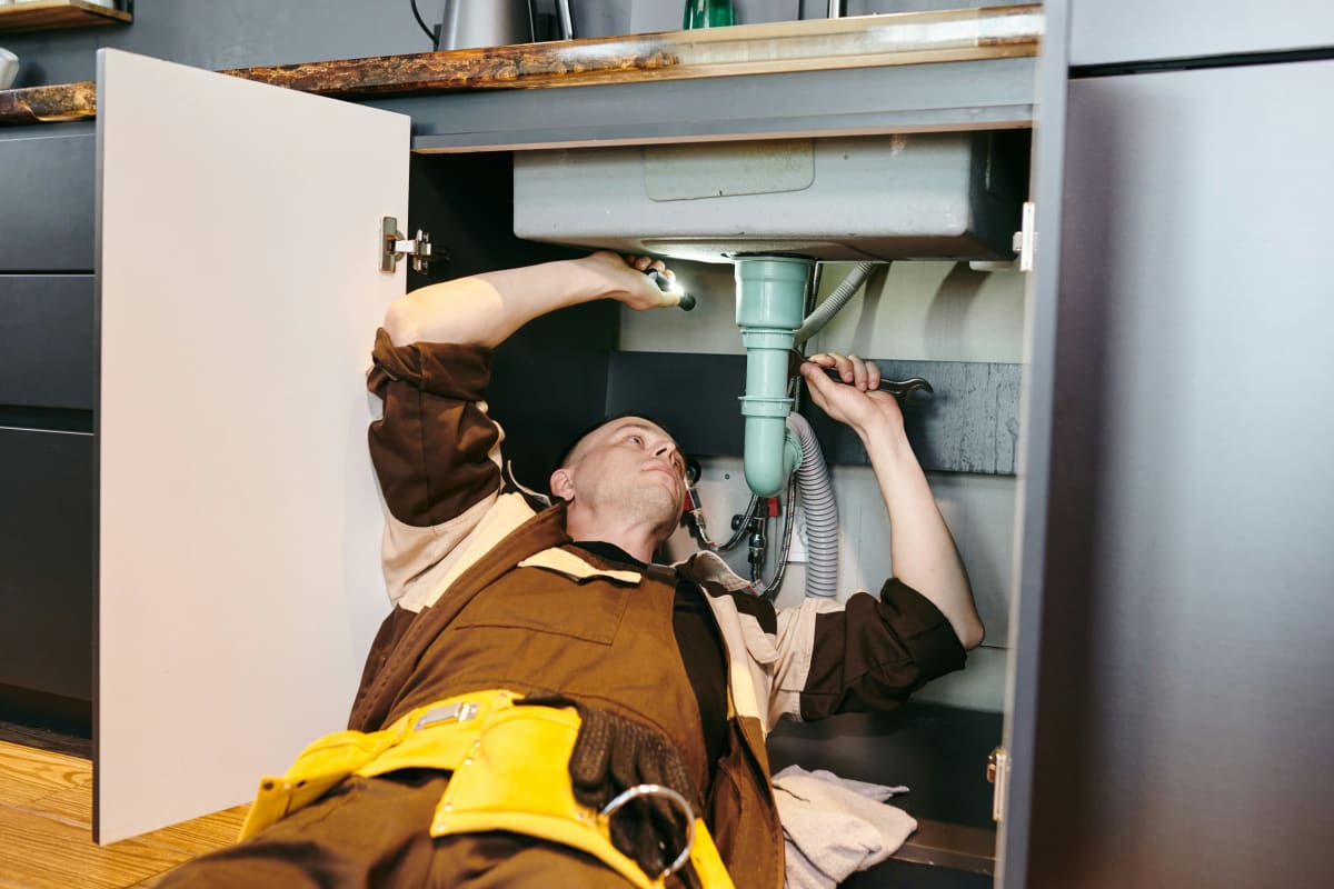 Plumber working on the drain under a kitchen sink