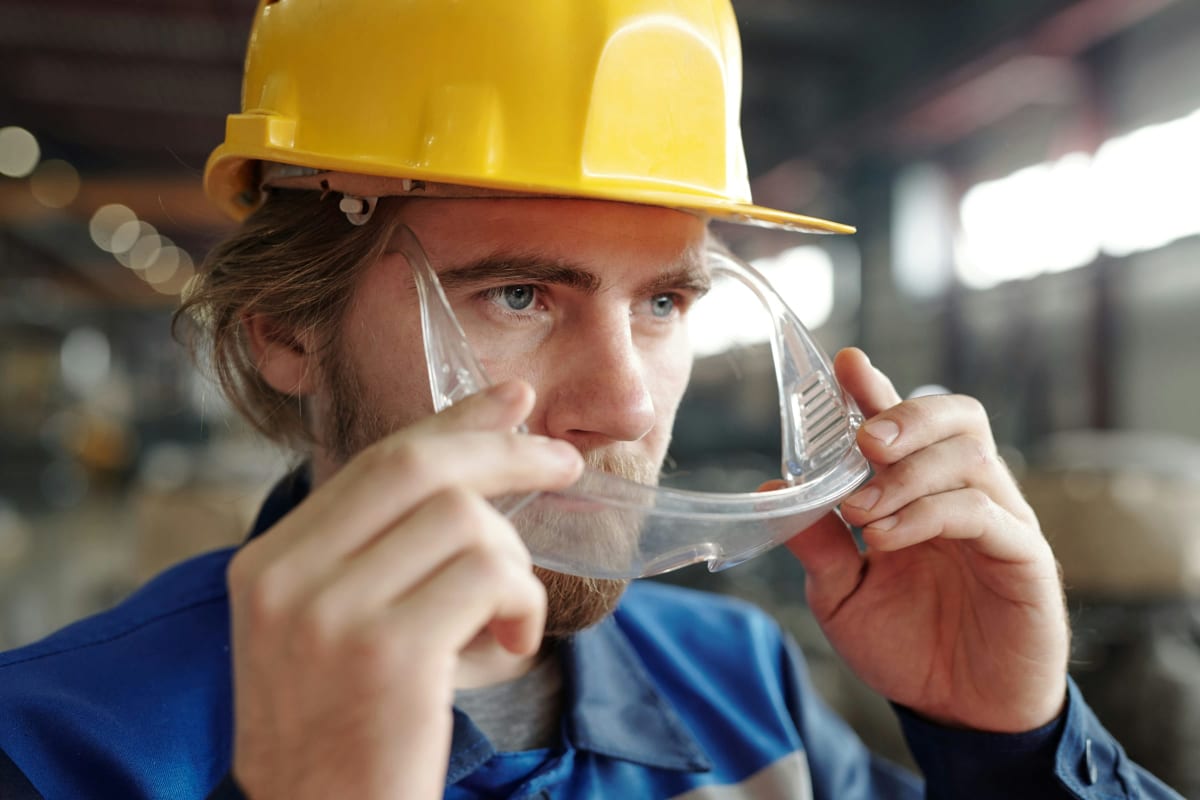 Worker in a hard hat putting on clear safety glasses