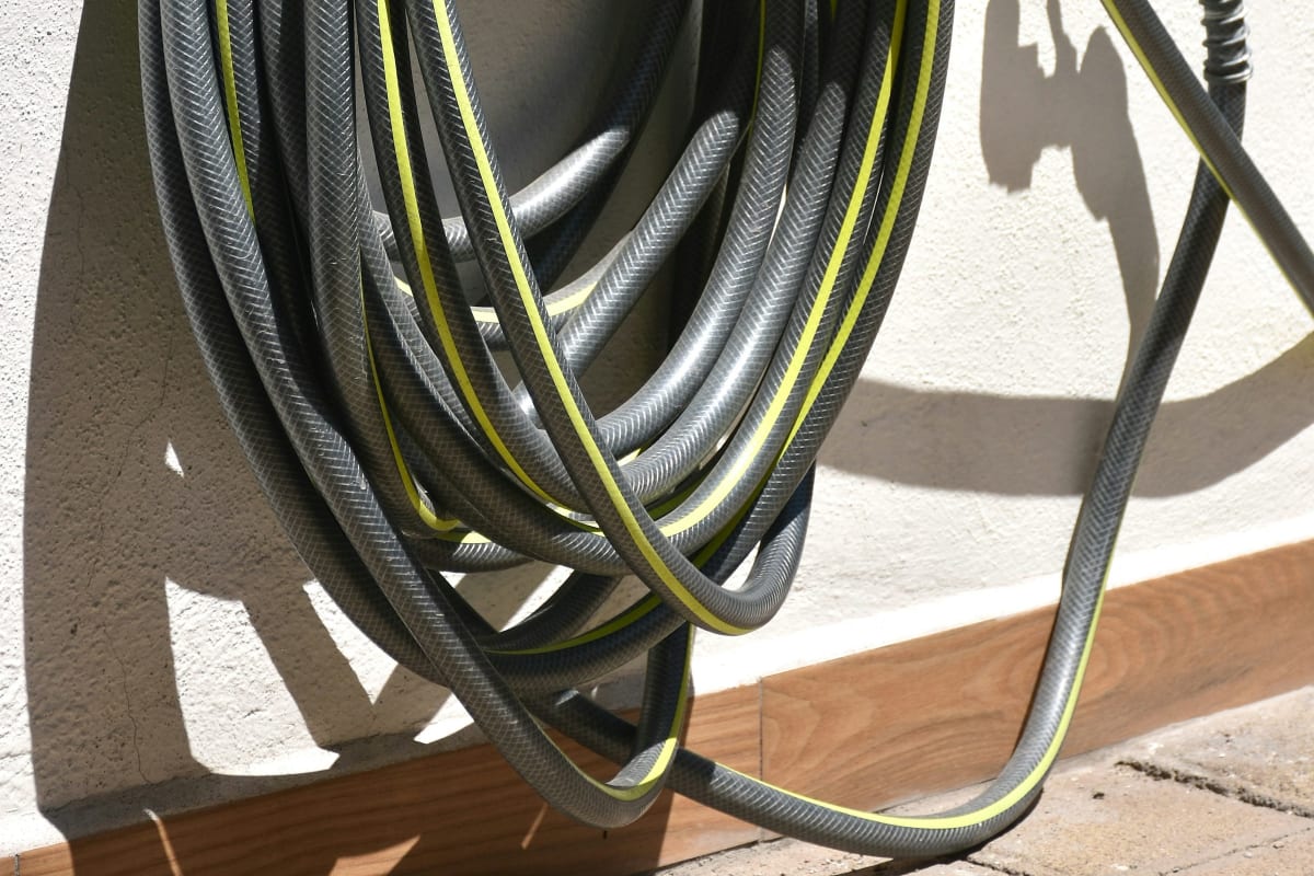 Garden hose coiled on a wall hanger by the spigot