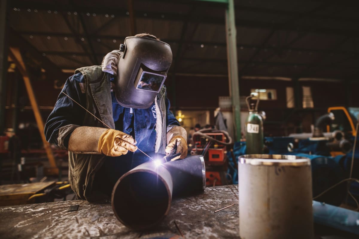 Welder in a helmet welding pipe in a shop
