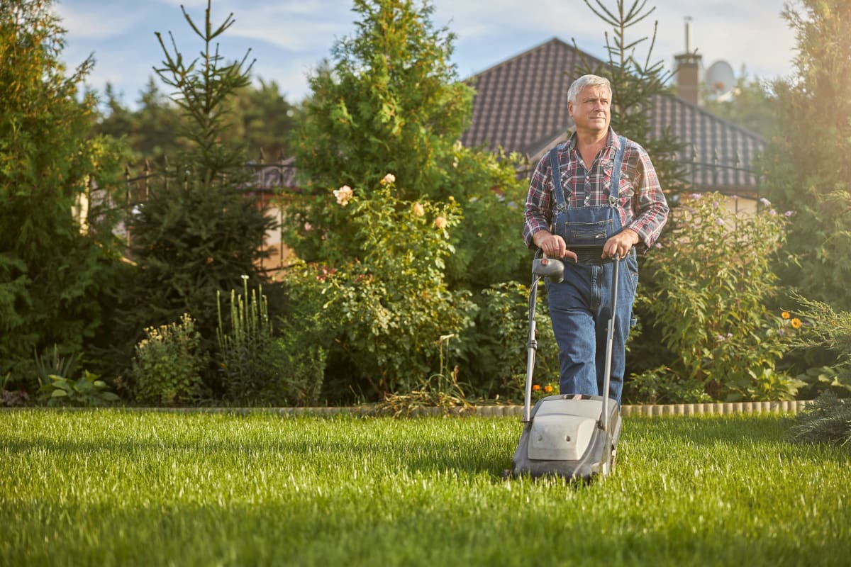Man mowing a thick green lawn in front of a house