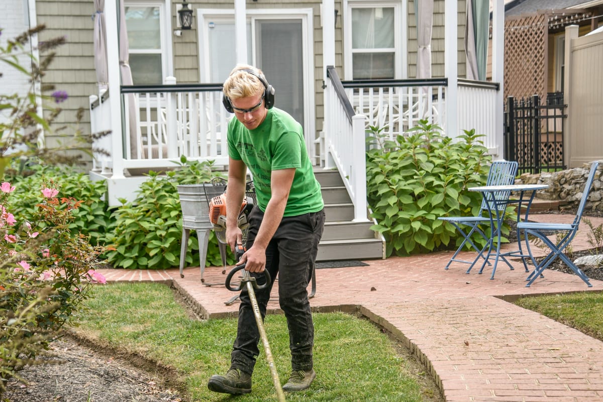 Homeowner trimming the lawn edge along a brick path