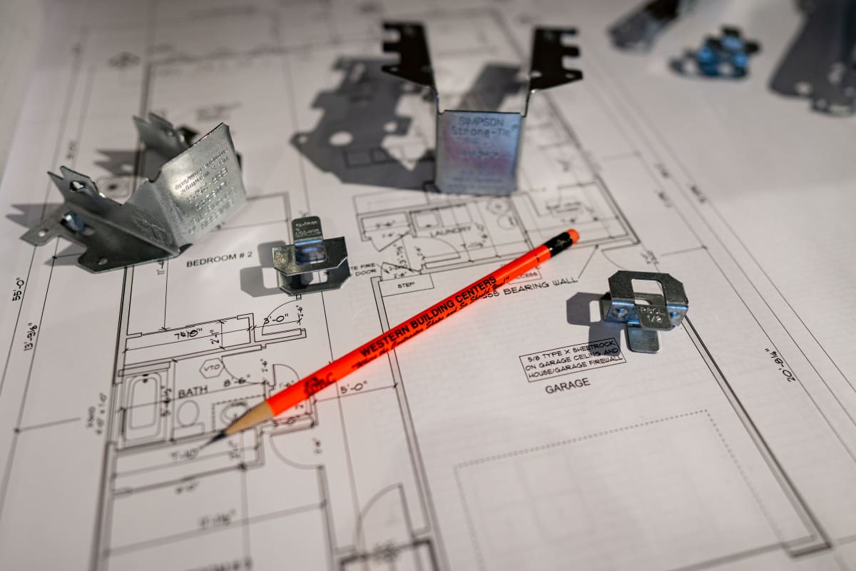Simpson Strong-Tie joist hangers and framing connectors laid out on a set of house plans with a carpenter pencil