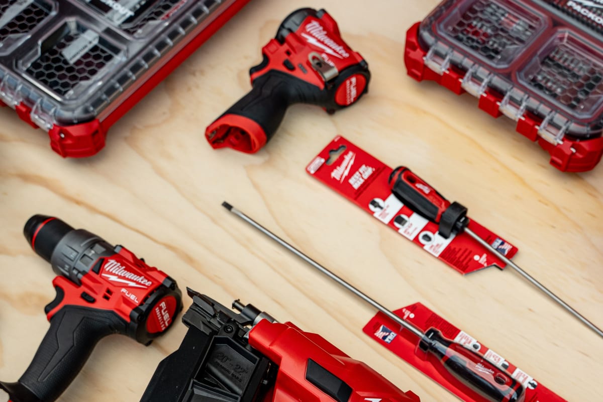 Milwaukee FUEL drills, nailer, bits and PACKOUT organizers laid out on a wood table