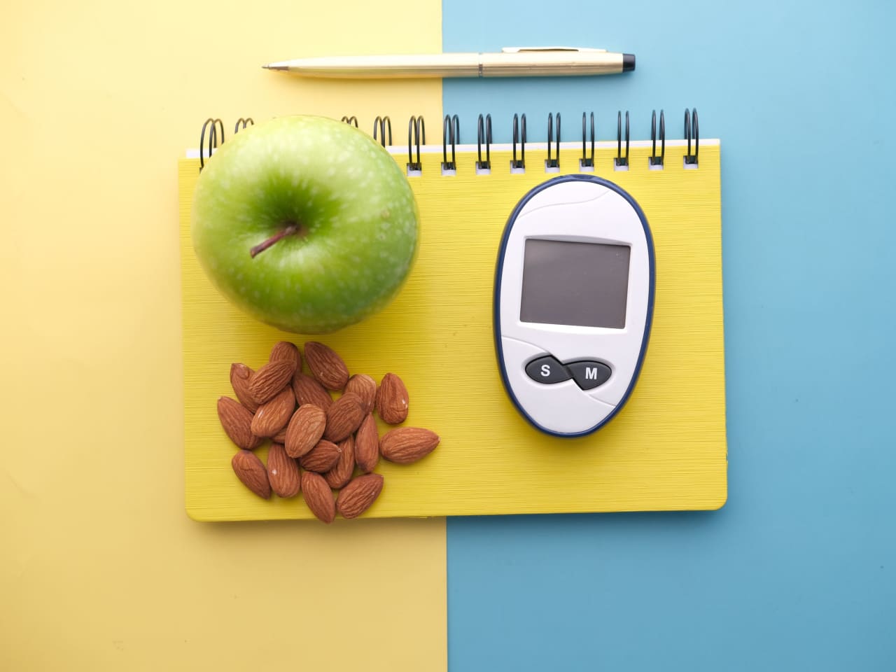 Glucose meter beside an apple and almonds on a notebook
