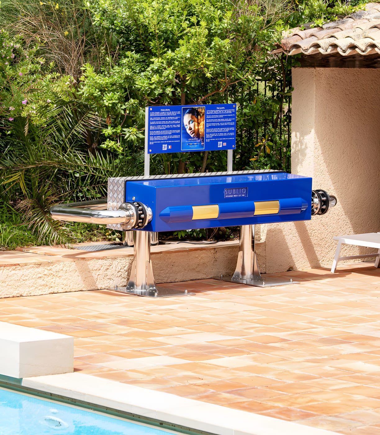Nahaufnahme des Sublio-Reaktors, blaues Gehäuse mit goldenen Bändern auf Edelstahlfüßen, am Pool des La Ferme d'Augustin