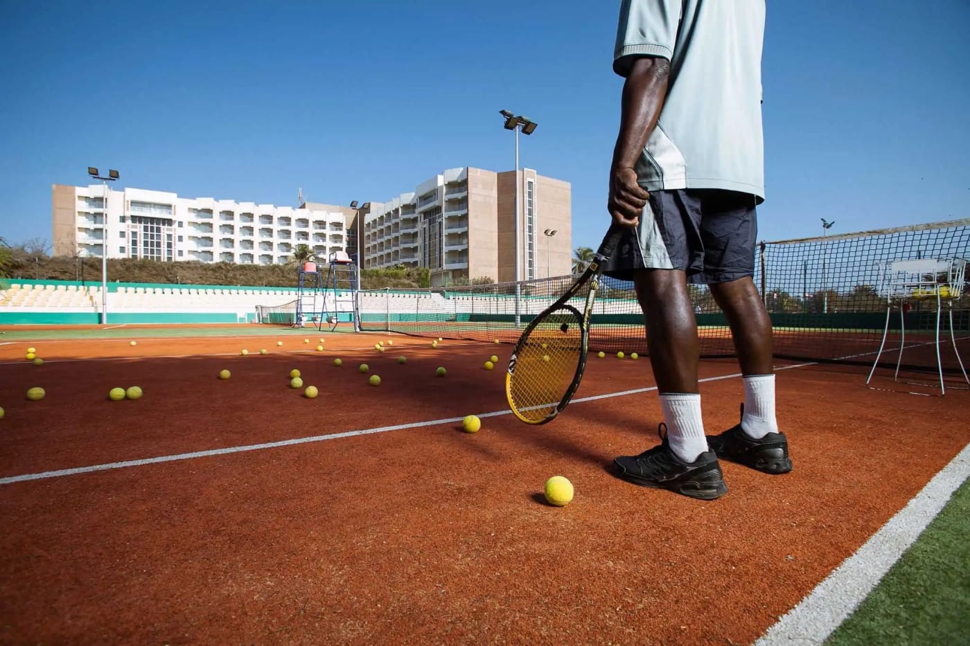 Jogador na quadra de tênis de saibro do King Fahd Palace, com o hotel ao fundo