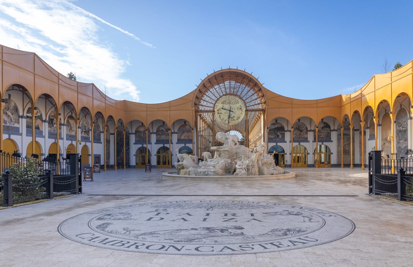 Der Eingangsplatz von Pairi Daiza mit gelben Arkaden und großer Uhr in Brugelette