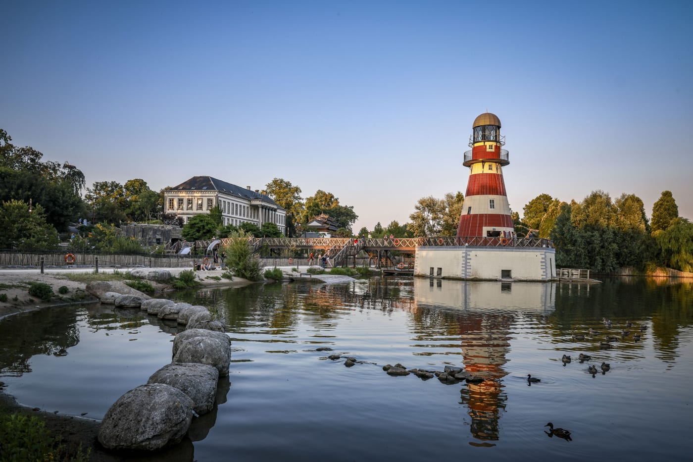 Der rot-weiße Leuchtturm von Cambron-sur-Mer spiegelt sich bei Sonnenuntergang im See von Pairi Daiza