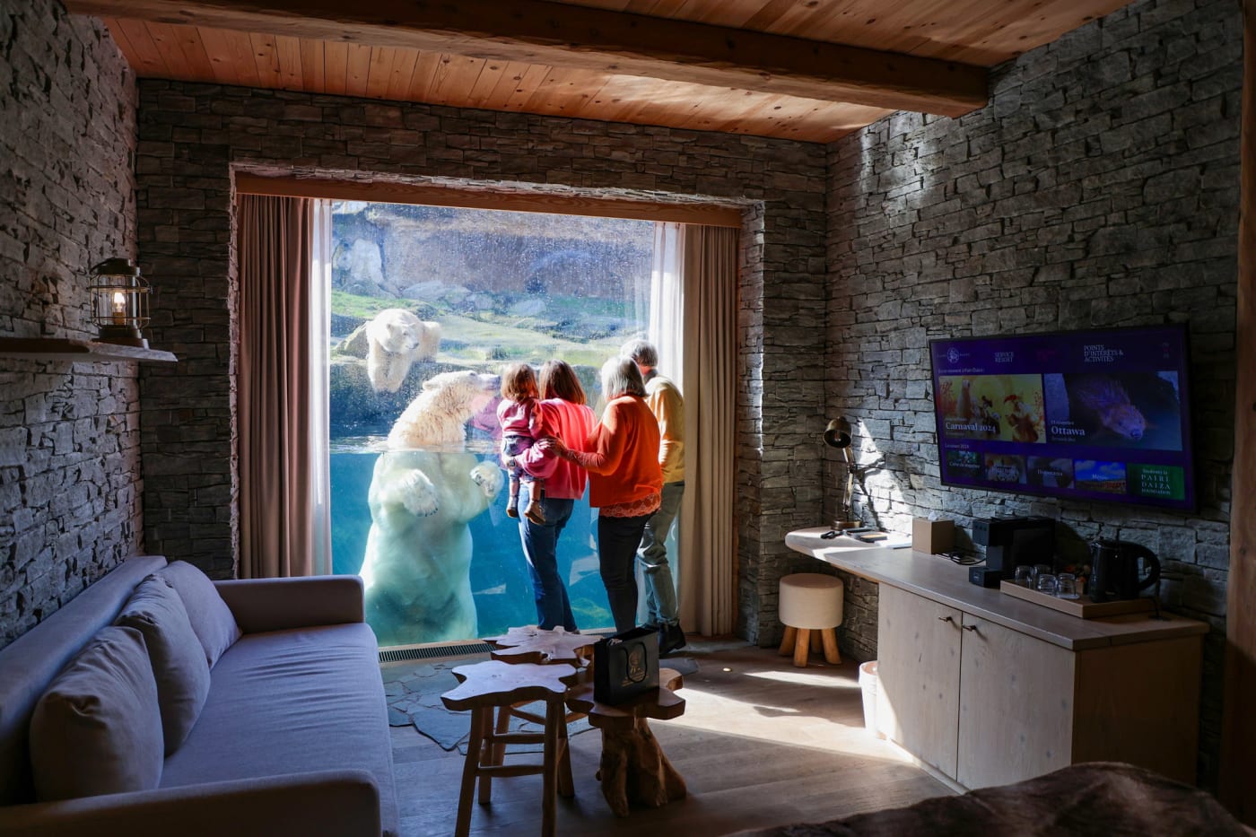 Eine Familie beobachtet einen Eisbären durch die Panoramascheibe eines Zimmers im White Bear House