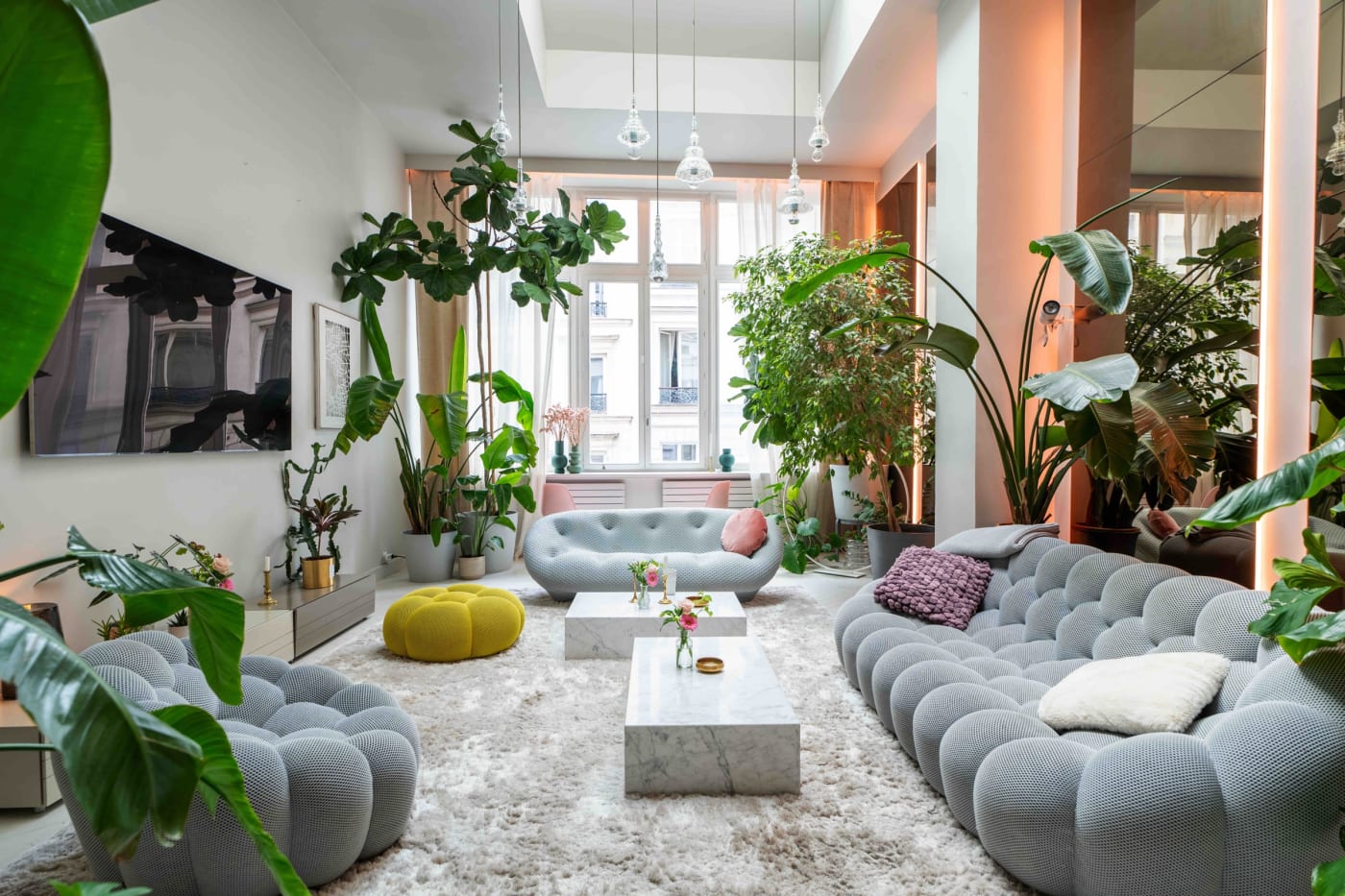 El salón lleno de vegetación del apartamento de diseño, con sofás grises y grandes plantas, entre los distritos 9 y 10
