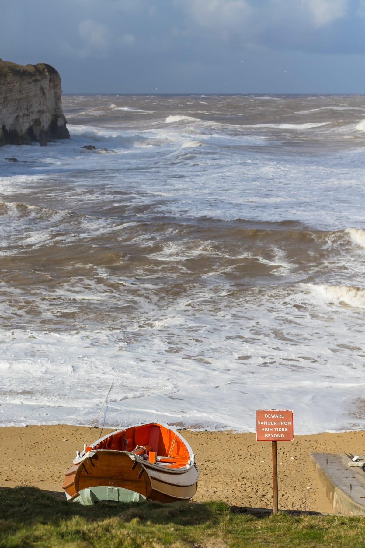 Orange boat and warning sign above a rocky Flamborough shore