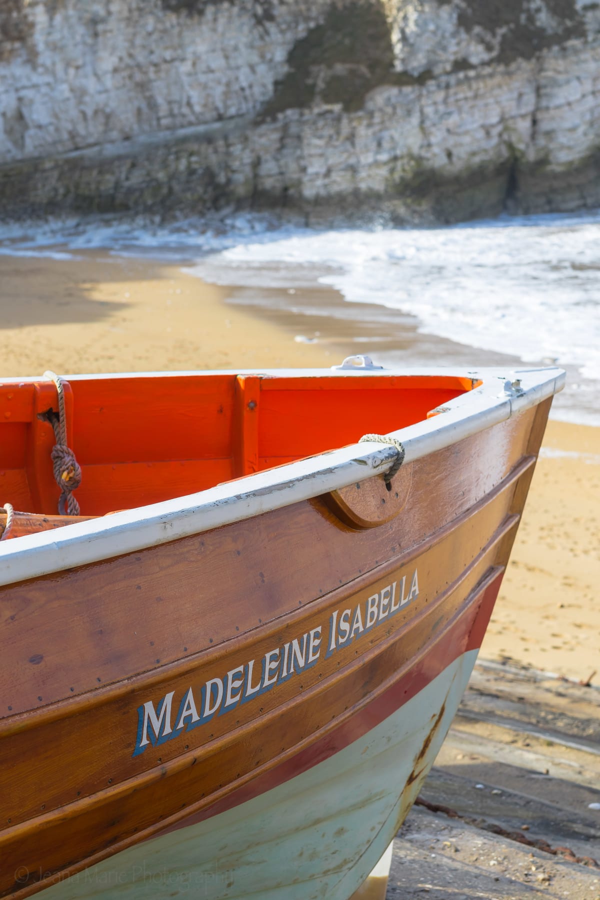 Bow of the orange Madeleine Isabella boat beside a sandy cove