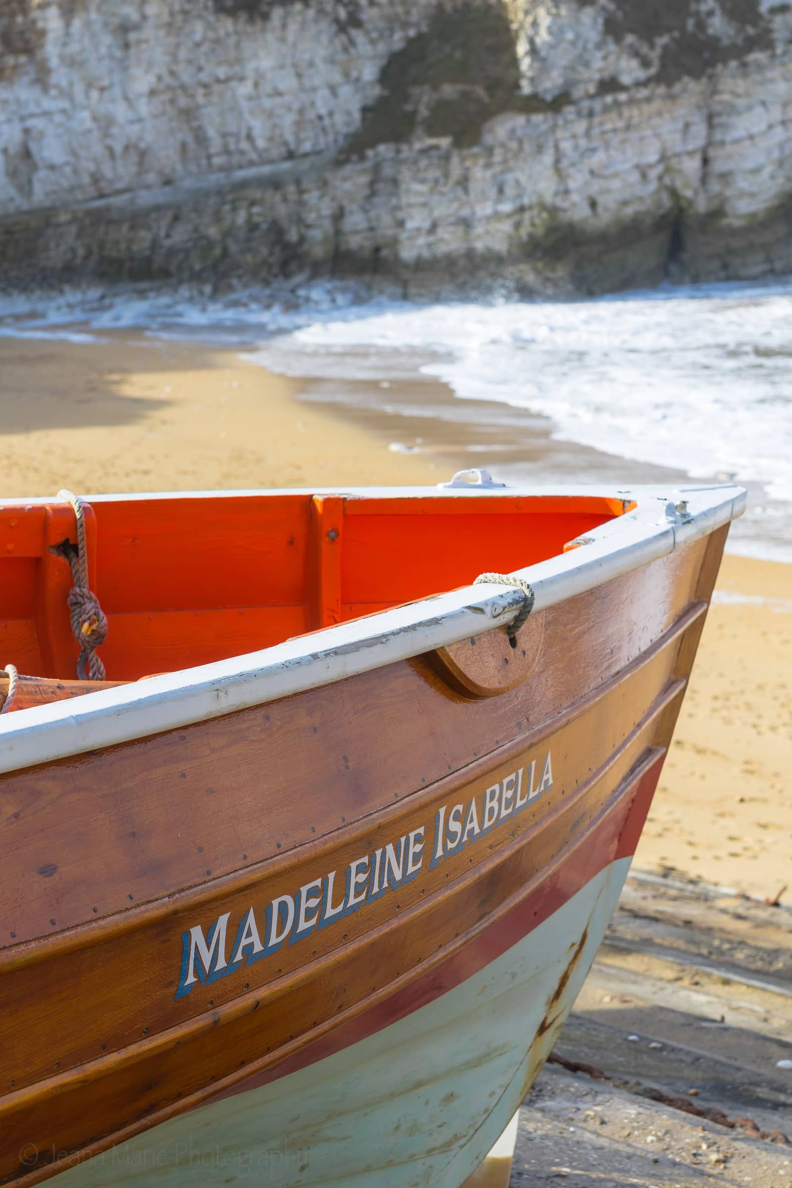 Bow of the orange Madeleine Isabella boat beside a sandy cove