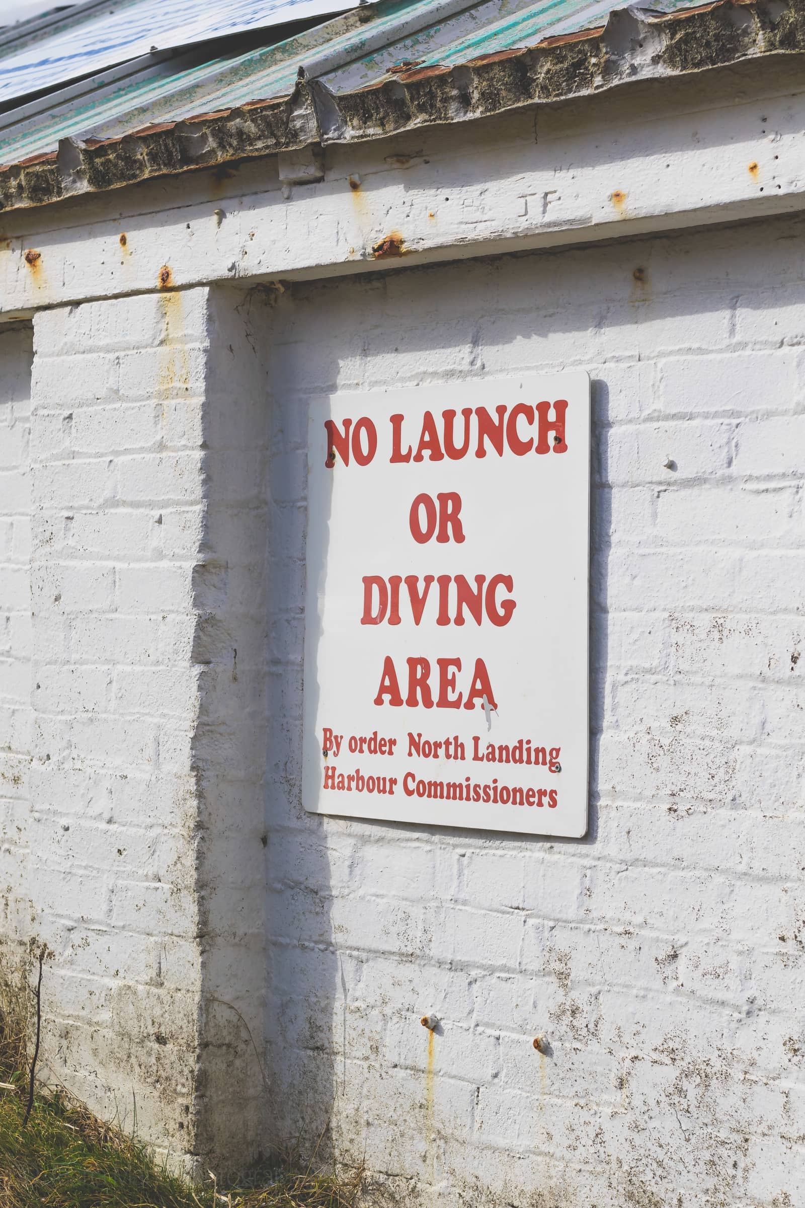 Red no launch or diving sign on a weathered white wall