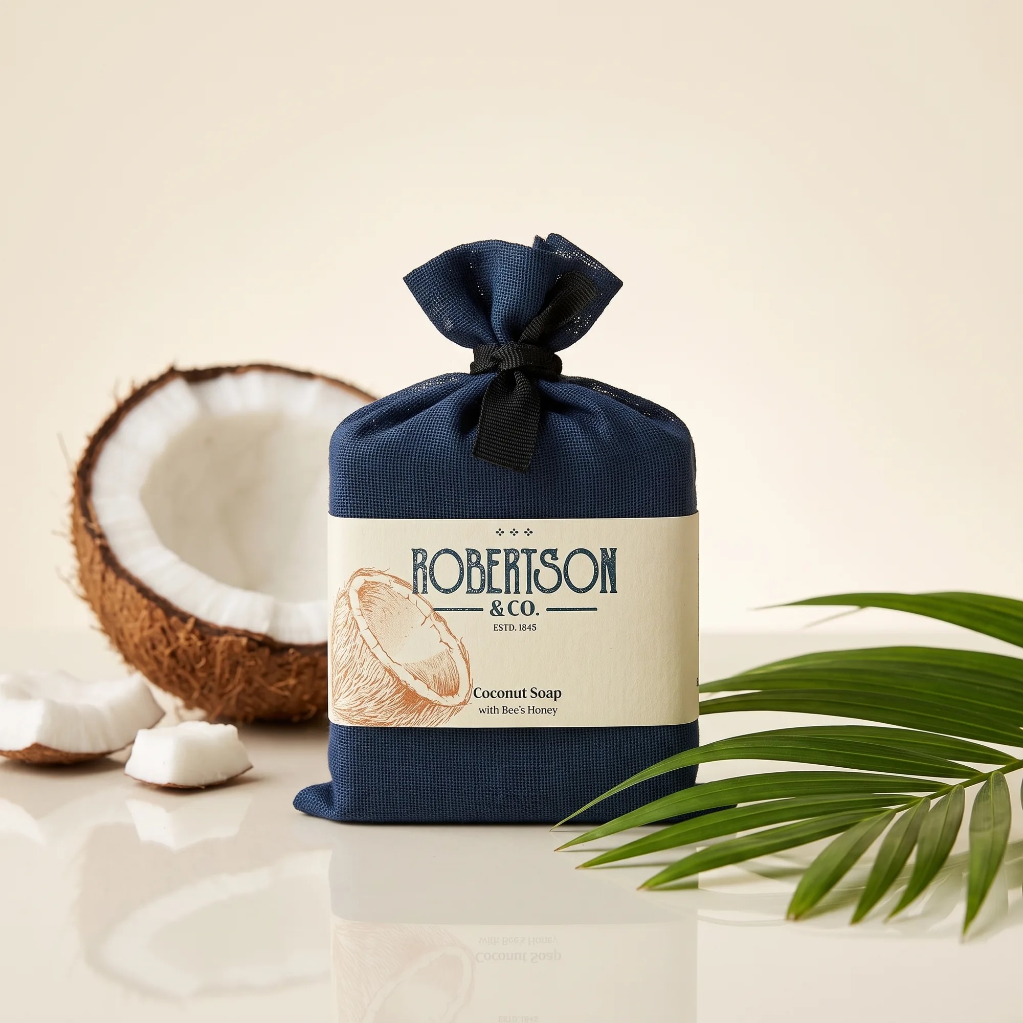 Coconut Soap 100g bar soap in a cotton drawstring pouch on a reflective glass surface — made in Sri Lanka, from Agromel UK