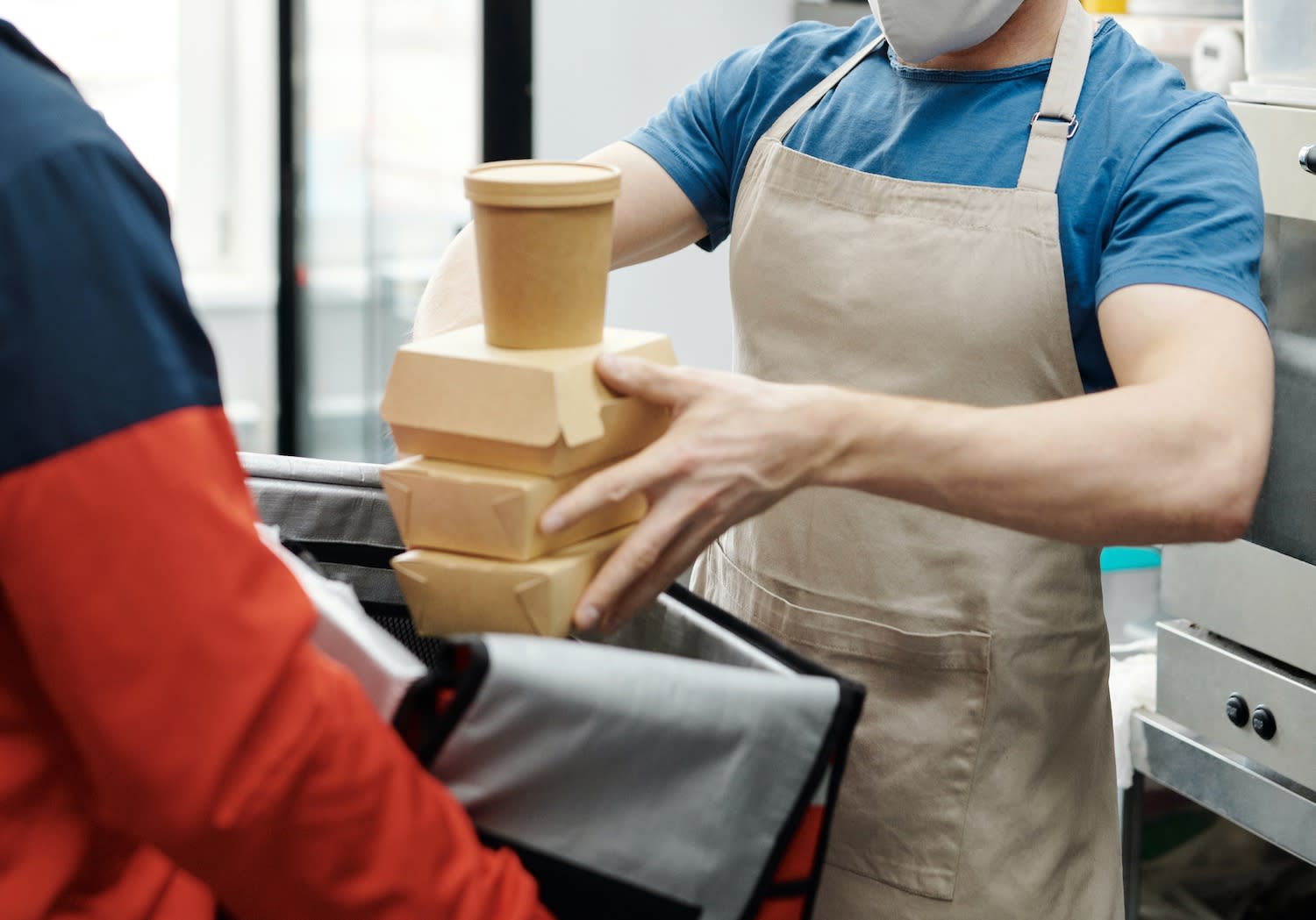 Restaurant worker hands food to delivery man. Article for Table Sage