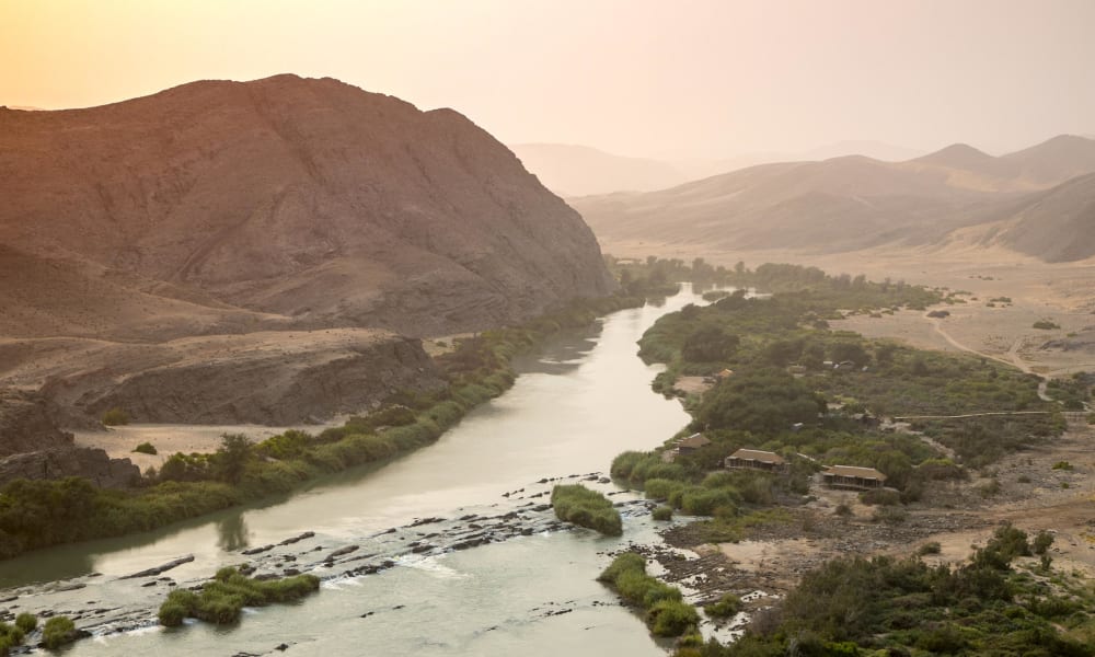 Eine malerische Wüstenlandschaft in Namibia, durchzogen von einem ruhigen Fluss, der sich durch das karge, felsige Terrain schlängelt.