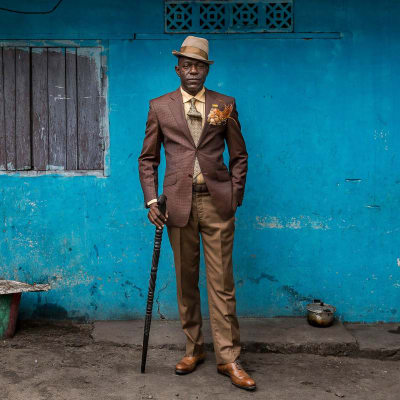 Mann aus Brazzaville steht mit einem Gehstock vor einer blauen Mauer