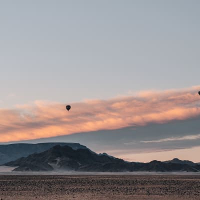 Sonnenaufgang über der Wüstenlandschaft Namibias mit zwei Heißluftballons in der Luft