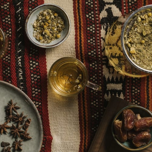 There is a table covered with a blanket, on the table in the middle is oil and around it other spices and dates.