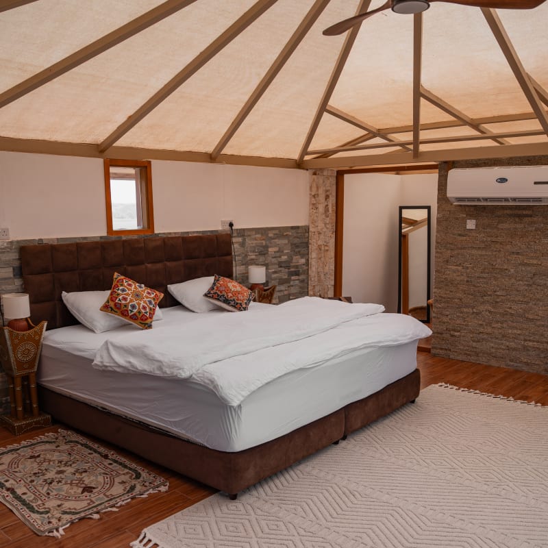 Gemütliches Schlafzimmer in einem Zelt mit einem großen Bett, weißen Bettlaken, dekorativen Kissen, einem Deckenventilator und einem Teppich auf Holzboden.