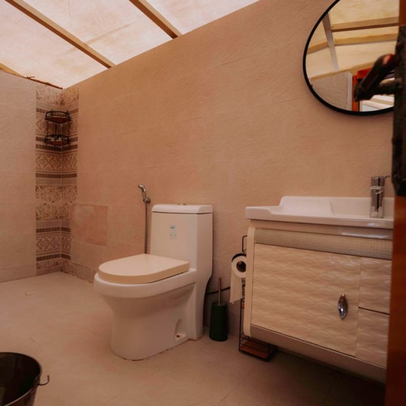 Badezimmer in einem Bungalow mit Toilette, Waschbecken im Unterschrank und einem runden Spiegel an der Wand.