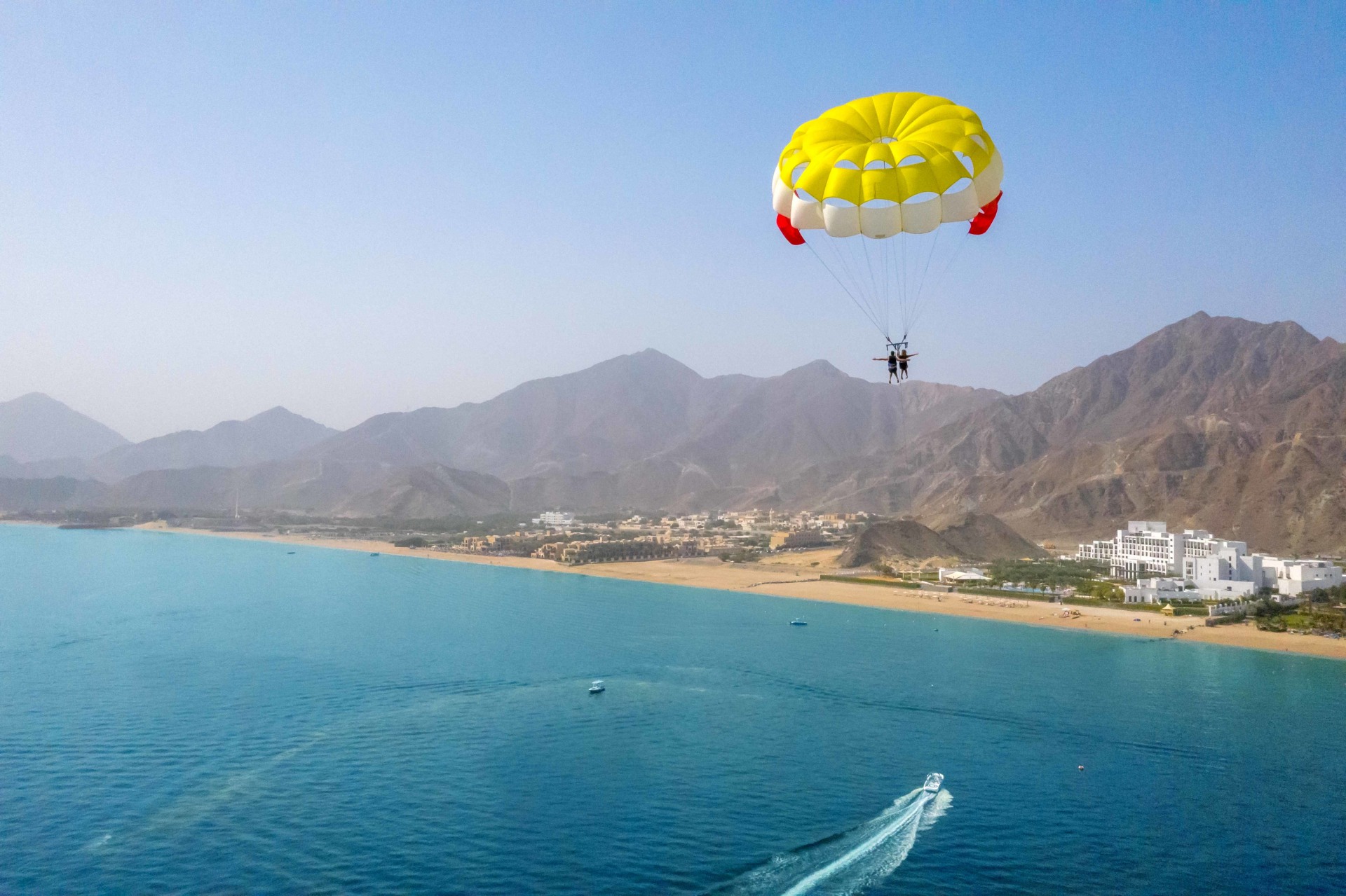 Luftaufnahme des Meeres mit Hotelanlage und Paraglider