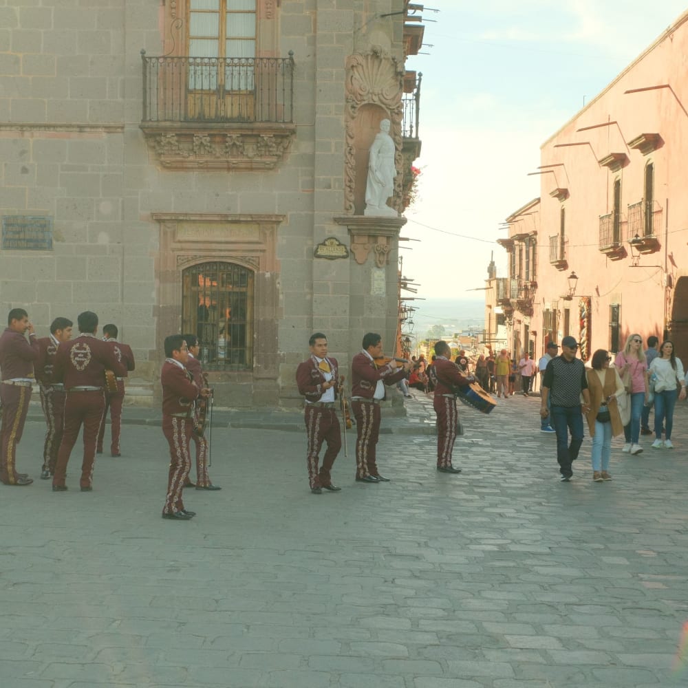 Mariachi-Musiker in traditionellen Kostümen spielen Instrumente auf einer gepflasterten Straße in einem historischen Stadtkern mit kolonialen Gebäuden.