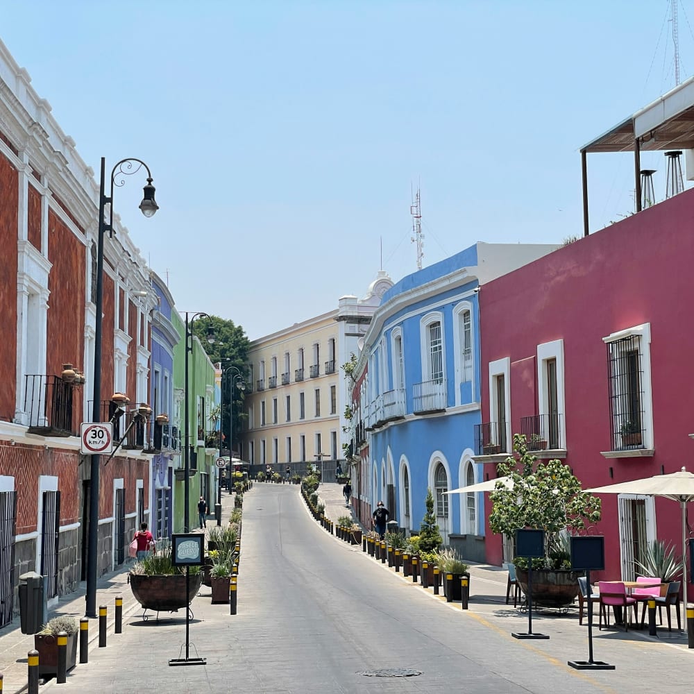 Ruhige Straße in Puebla, Mexiko, gesäumt von bunten kolonialstil Häusern mit roten, grünen, blauen und violetten Fassaden unter klarem blauem Himmel.