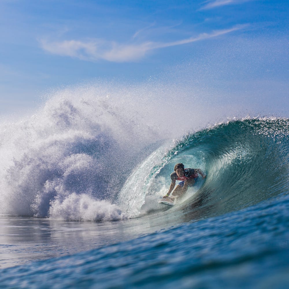 Ein Surfer reitet in einer großen brechenden Welle bei Puerto Escondido unter klarem blauem Himmel.
