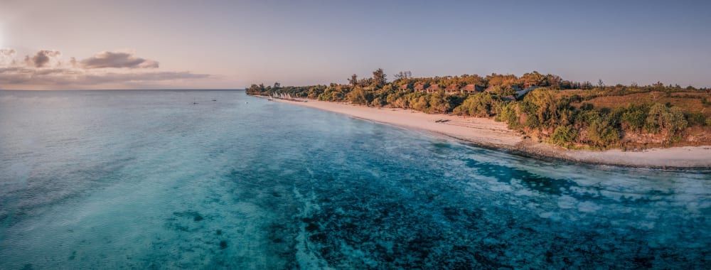 Luftaufnahme des Manta Resorts auf Pemba Island mit klarem türkisfarbenem Wasser und einer üppigen Küstenlinie mit tropischen Bäumen.