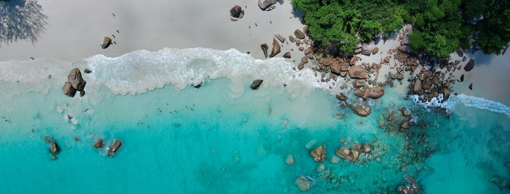An aerial view of a pristine beach with white sand, turquoise waters, and dense green trees.