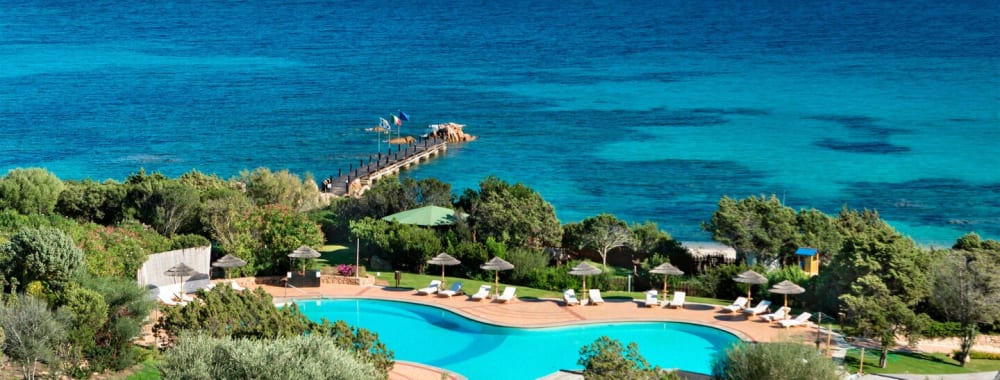 Ein großes Hotel mit einem Swimmingpool, umgeben von grünen Bäumen und Blick auf das Meer.