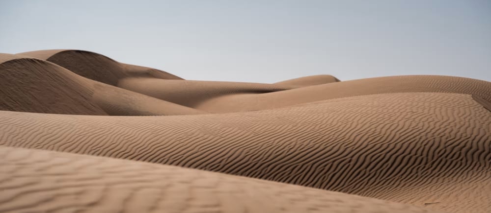 Große Sanddünen mit gezackten Texturen unter einem klaren Himmel.