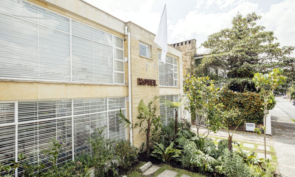 Modern two-story building with large glass windows, a white flag on a flagpole, and lush green landscaping in front.
