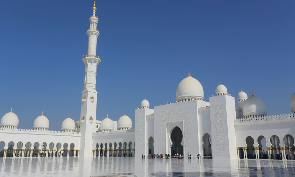 Majestic white mosque with domes and a tall minaret under a clear blue sky.