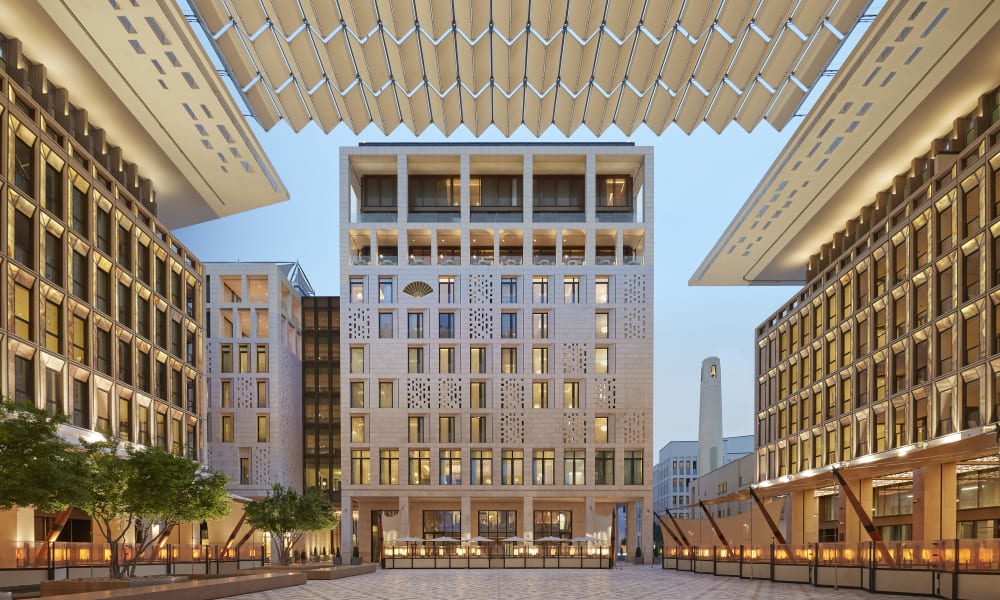 Ein moderner architektonischer Platz mit symmetrischen Gebäuden auf beiden Seiten und einem zentralen Hochhaus in Doha, Katar, mit dekorativen Dachstrukturen darüber.